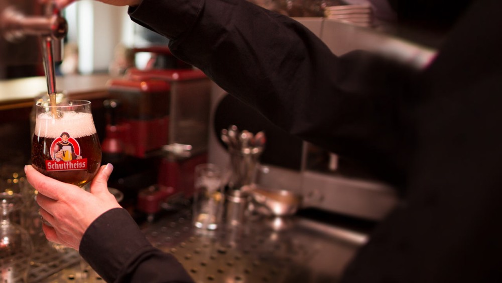 Eine Person zapft Bier in ein Glas an einer Bar. Das Bierglas hat ein Logo.