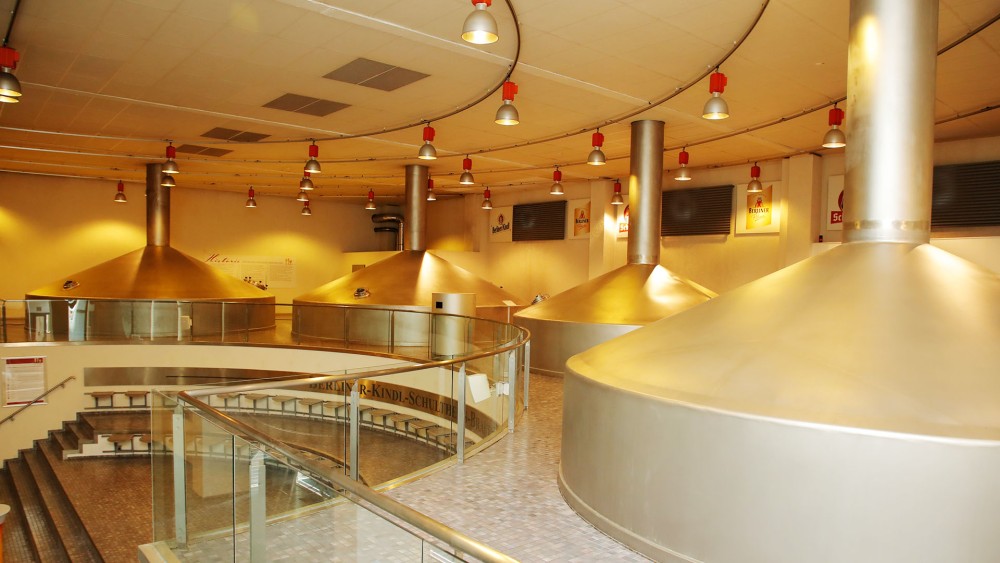 Große Metallkessel und Treppen in einer modernen Brauerei mit roten Hängelampen.