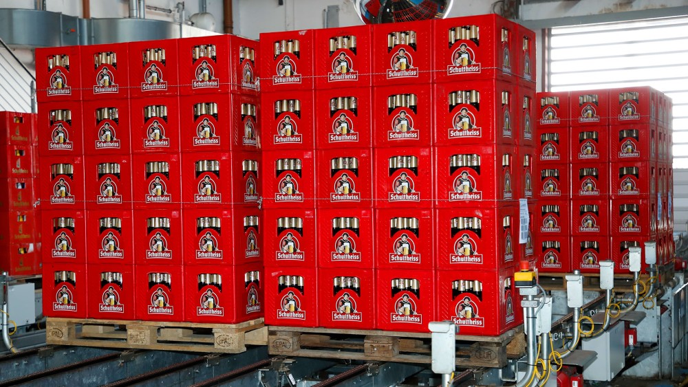 Mehrere gestapelte Getränkekisten stehen auf Paletten in einer Fabrikhalle.