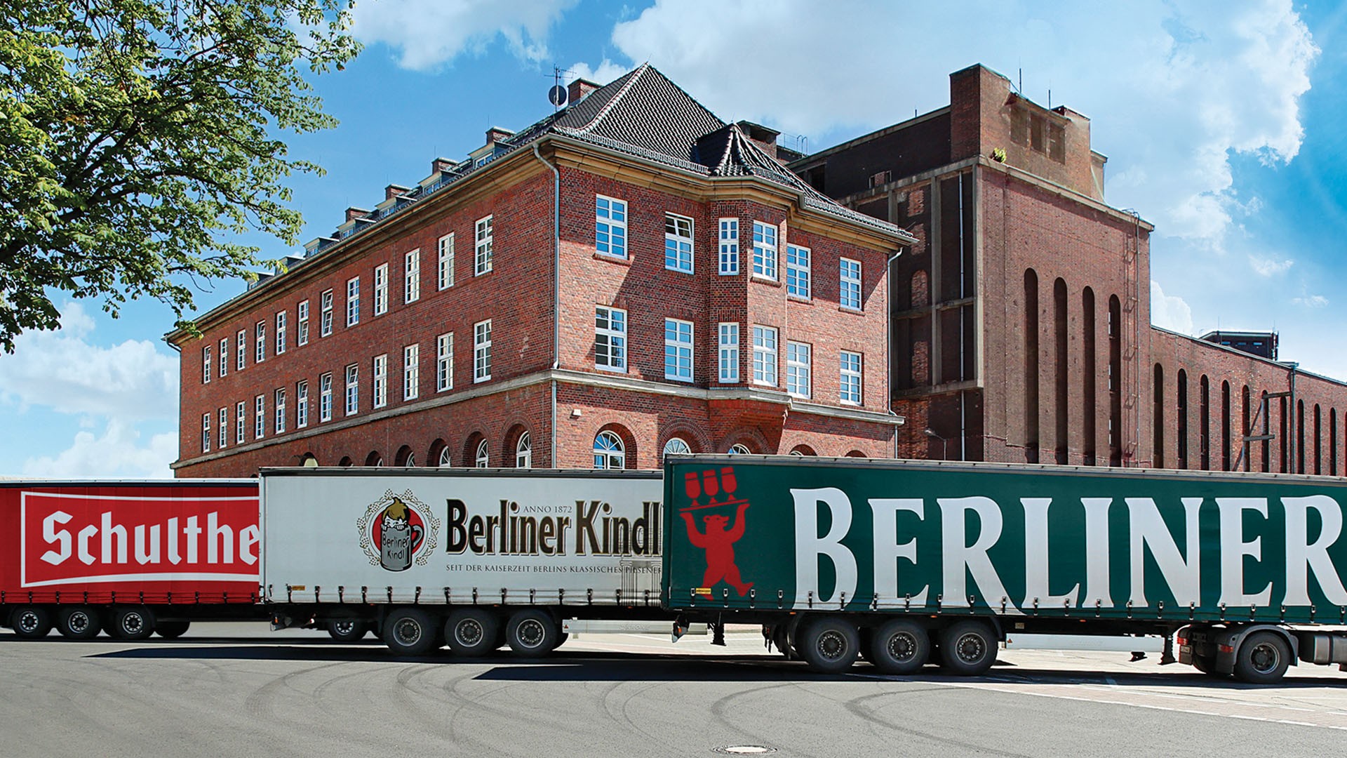 Drei LKW fahren vor einem historischen Backsteingebäude entlang.