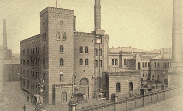 Historisches Foto einer alten Fabrik mit hohen Schornsteinen und festungsähnlicher Architektur.