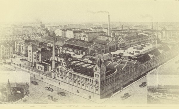 Eine historische Industrieanlage mit mehreren Gebäuden und Schornsteinen, umgeben von Straßen und Fuhrwerken.