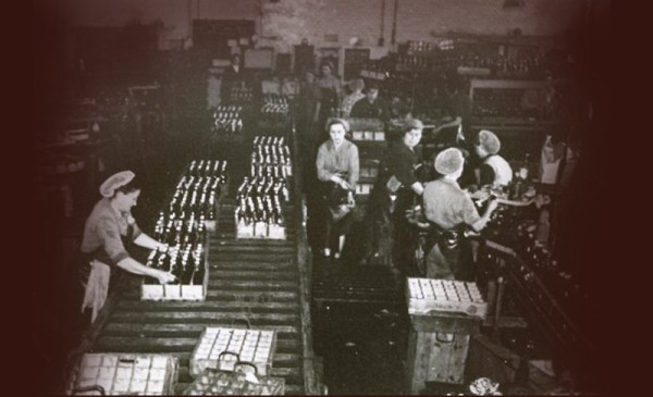 Mehrere Arbeiter sind in einer alten Fabrik tätig, sie verpacken Flaschen.