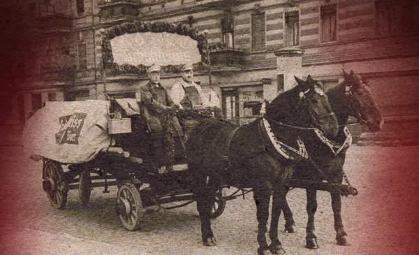 Zwei Männer fahren in einer von Pferden gezogenen Kutsche auf einer Straße.