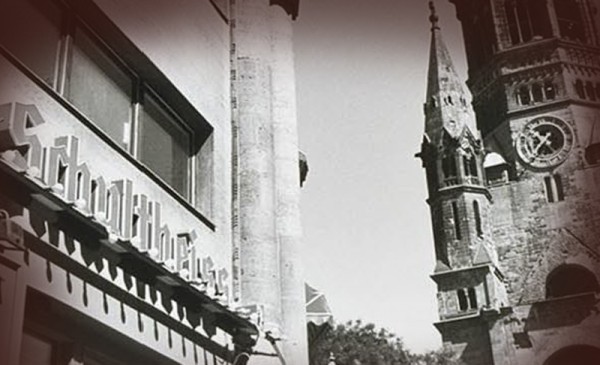 Ein historisches Gebäude mit dekorativer Beschriftung steht neben einem Turm mit Uhr.